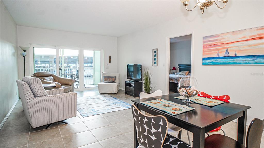 A dining area with a dark table and chairs opens into a living room with tile floors — 420 64TH AVENUE UNIT 101, ST PETE BEACH, FL