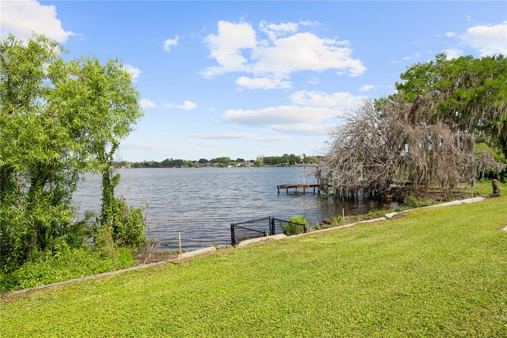 A grassy lawn slopes down to a lake with a small wooden dock and trees — 240 KILLARNEY DRIVE, WINTER PARK, FL