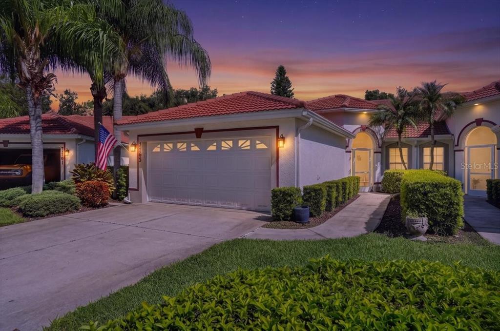 A single-story house with a two-car garage, red tile roof, and a landscaped front yard — 7165 MELROSE PLACE, BRADENTON, FL