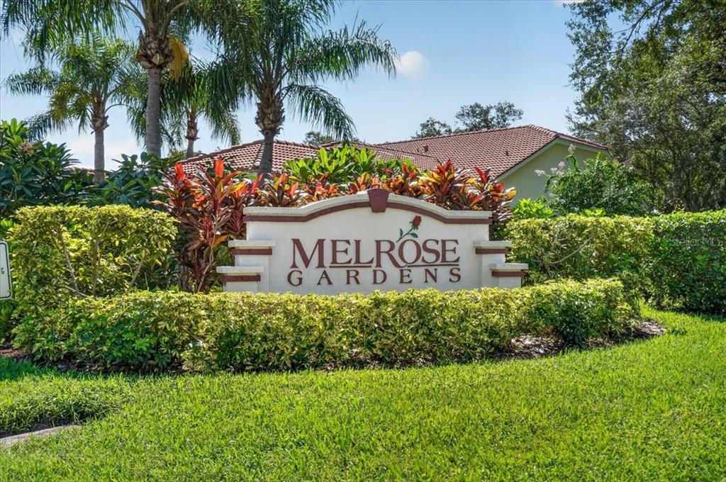 A stone monument sign for Melrose Gardens stands in front of lush landscaping and palm trees — 7165 MELROSE PLACE, BRADENTON, FL