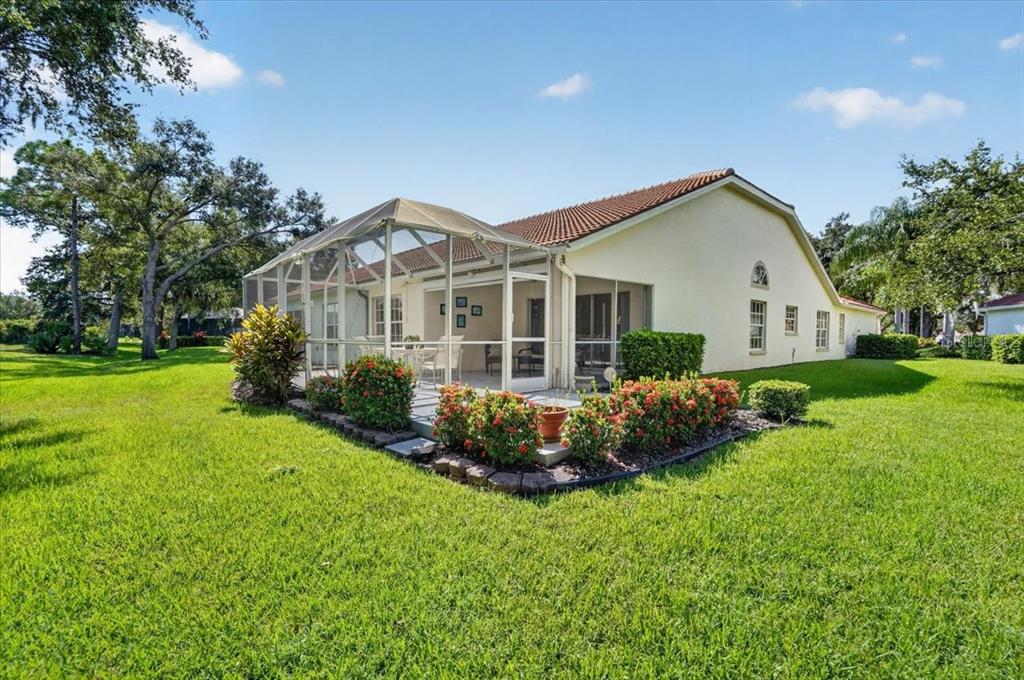 A beige house with a screened-in patio and a landscaped garden in a grassy yard — 7165 MELROSE PLACE, BRADENTON, FL