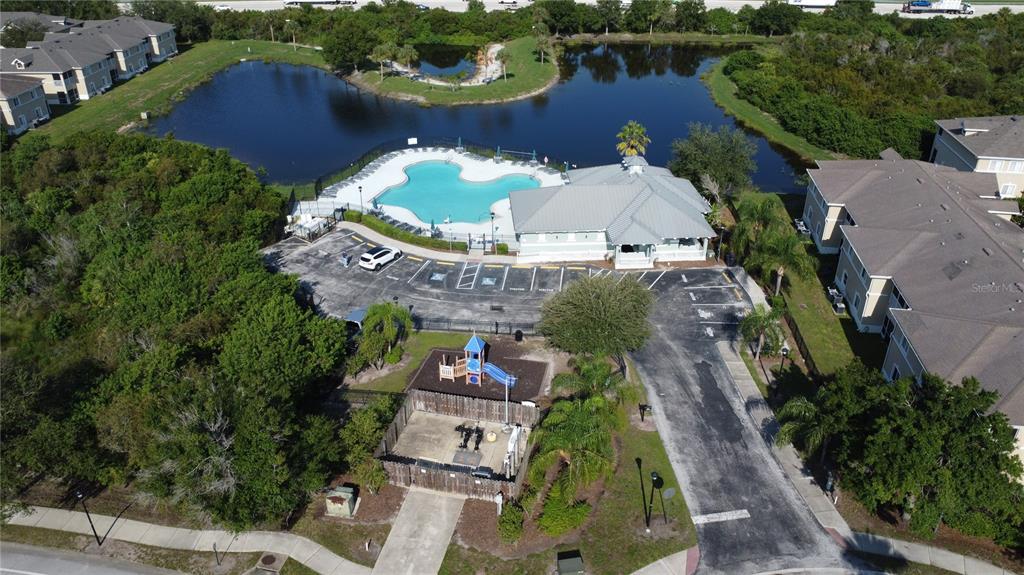 An aerial view shows a community swimming pool, clubhouse, playground, and parking lot near a lake — 9523 GROVEDALE CIRCLE UNIT 101, RIVERVIEW, FL