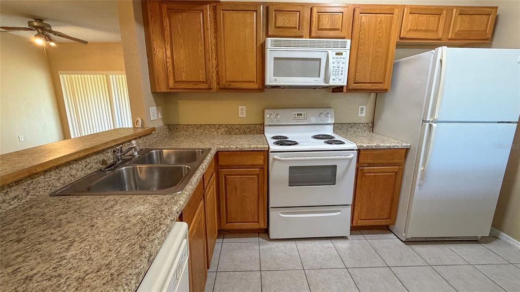 A kitchen features wood cabinets, white appliances, a double sink, and speckled laminate countertops — 9523 GROVEDALE CIRCLE UNIT 101, RIVERVIEW, FL