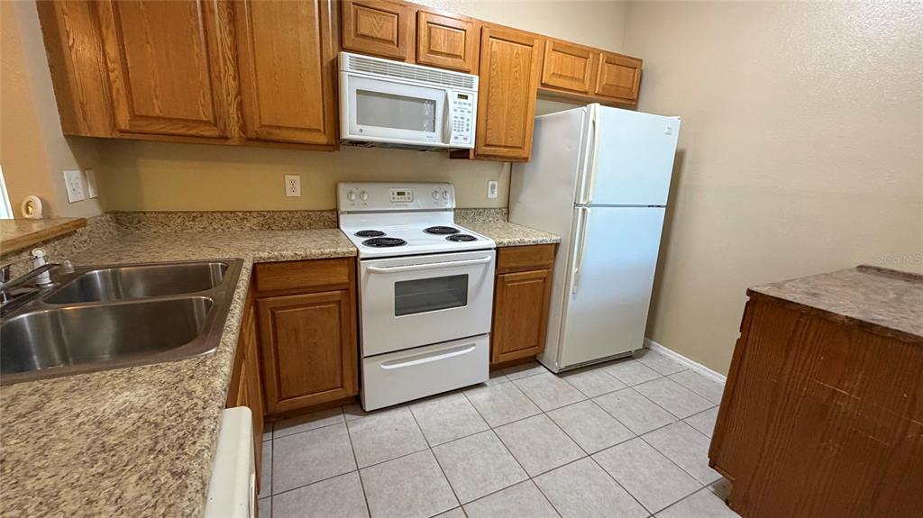 A kitchen features wood cabinets, white appliances, a double sink, and speckled laminate countertops — 9523 GROVEDALE CIRCLE UNIT 101, RIVERVIEW, FL