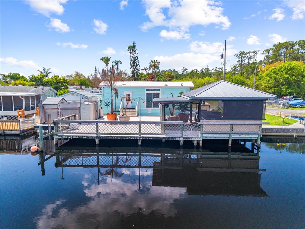 A light blue mobile home features a large wooden deck and a covered patio area — 1315 PINE ISLAND DR N, ST CLOUD, FL