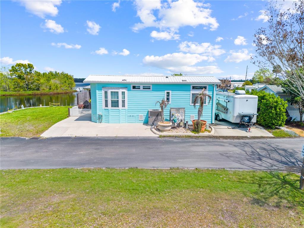 A light blue manufactured home sits next to a body of water with a trailer parked — 1315 PINE ISLAND DR N, ST CLOUD, FL