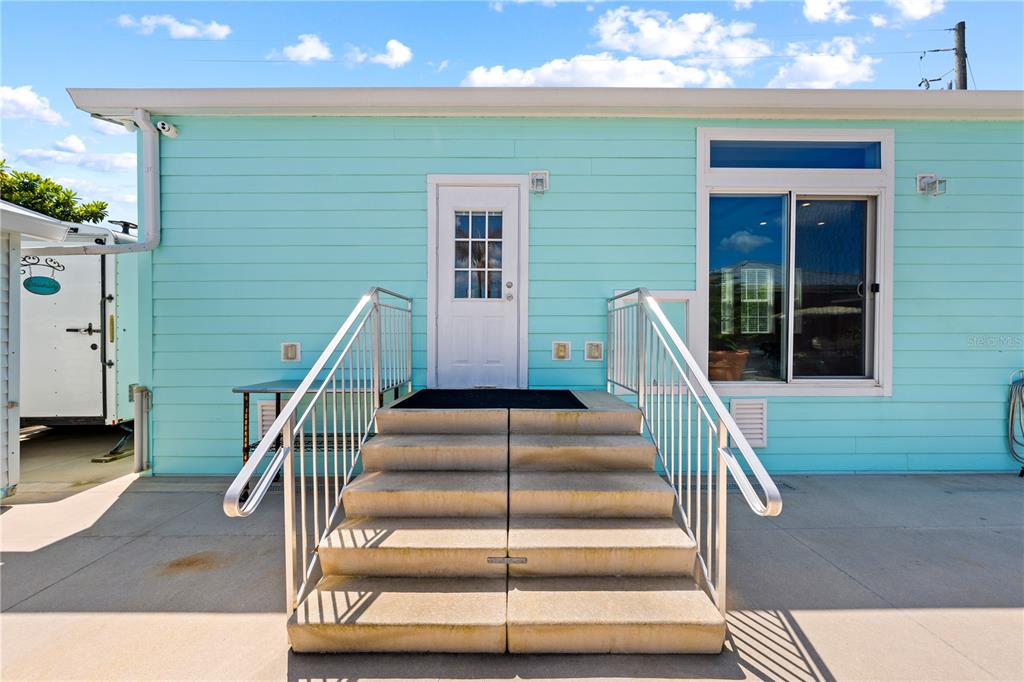 A light blue house exterior features a white door, concrete stairs, and a metal railing — 1315 PINE ISLAND DR N, ST CLOUD, FL