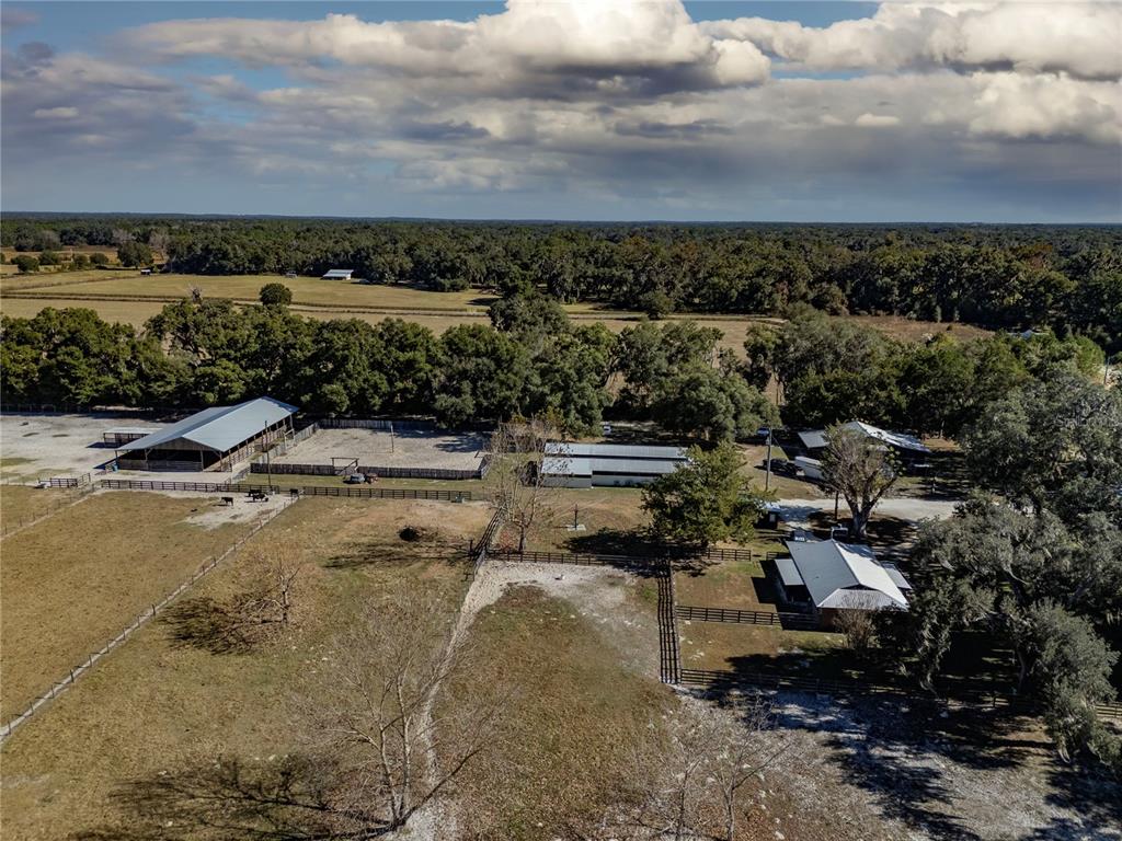 An aerial view of a rural property featuring multiple barns, fenced pastures, and surrounding trees — 17885 NE 2ND PLACE, WILLISTON, FL