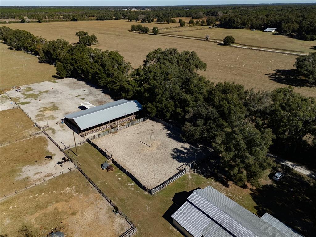 An aerial view shows a fenced riding arena and two metal-roofed barns on a rural property — 17885 NE 2ND PLACE, WILLISTON, FL