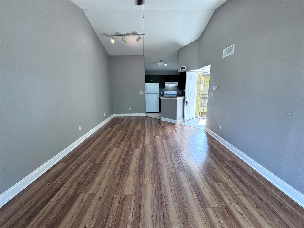 An empty living room with gray walls and wood-look flooring leads to a small kitchen — 1916 LAKE ATRIUMS CIRCLE UNIT 33, ORLANDO, FL