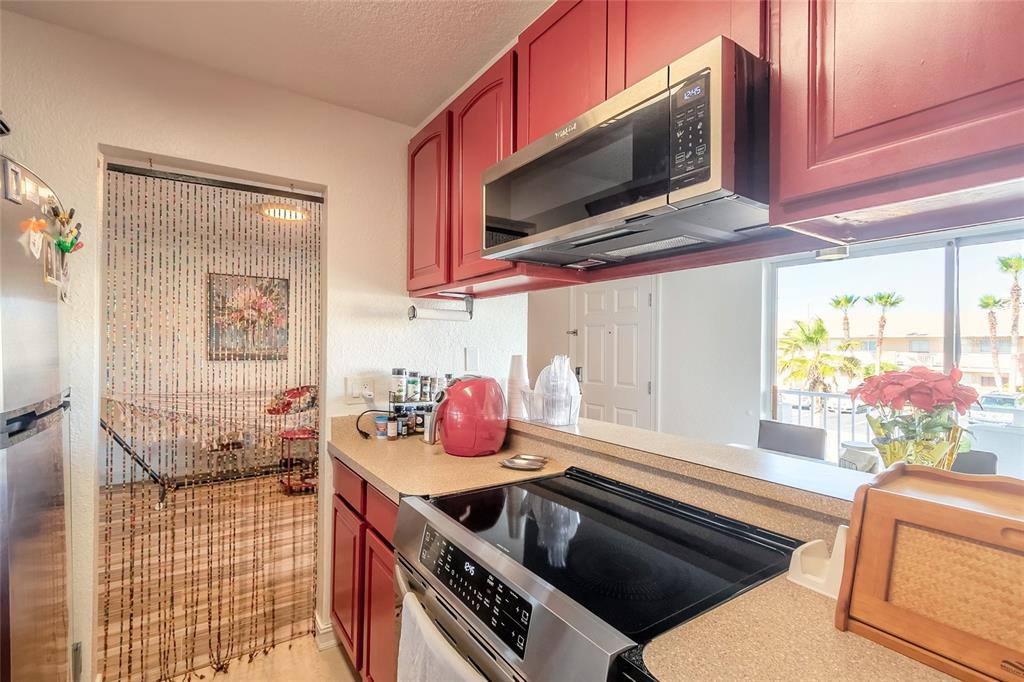 A kitchen with red cabinets, stainless steel appliances, and a pass-through window to a balcony — 428 AUBURN DRIVE UNIT 202, DAYTONA BEACH, FL