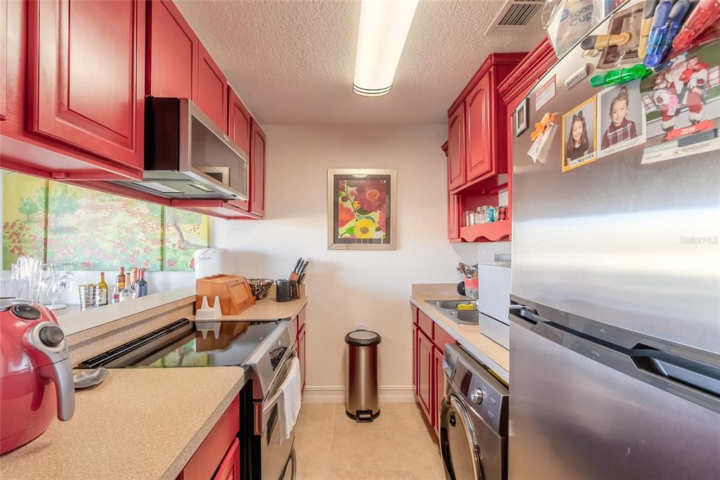 A galley kitchen features red cabinets, stainless steel appliances, and a beige countertop — 428 AUBURN DRIVE UNIT 202, DAYTONA BEACH, FL