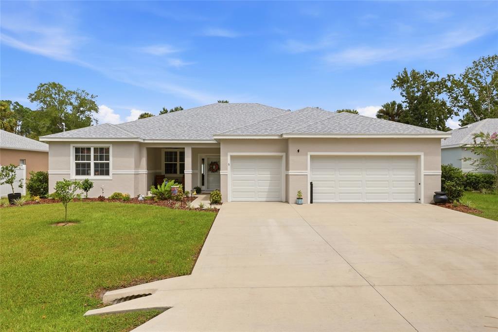 A single-story house with a beige exterior, a gray shingled roof, and a three-car garage — 5 PINE BUSH LANE, PALM COAST, FL