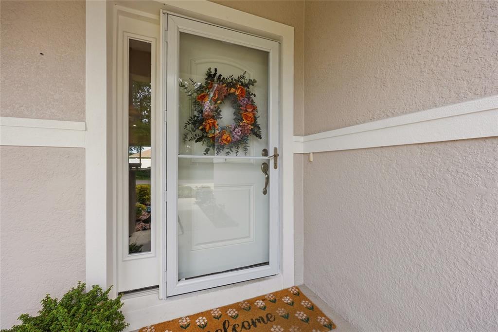 A white front door with a storm door and a floral wreath sits under a porch — 5 PINE BUSH LANE, PALM COAST, FL
