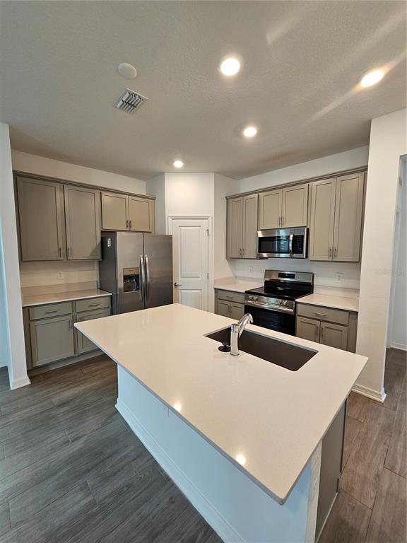 A kitchen features gray cabinets, stainless steel appliances, a white island, and wood-look tile flooring — 4123 CONJUNCTION WAY, APOPKA, FL