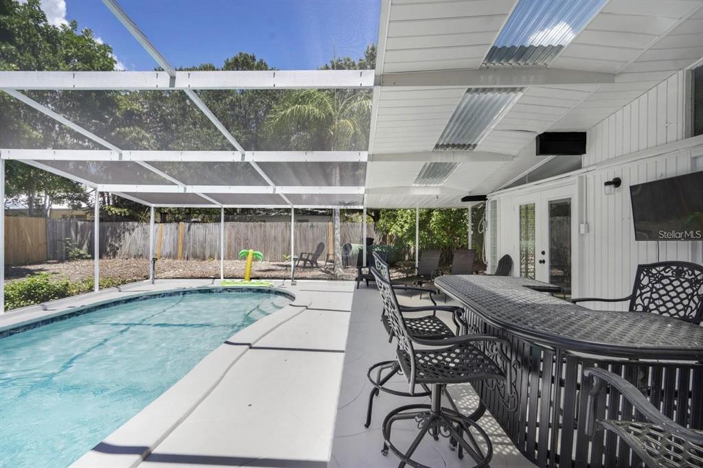 A screened-in patio features a swimming pool, a bar with stools, and a television — 2213 WASON ROAD, SARASOTA, FL