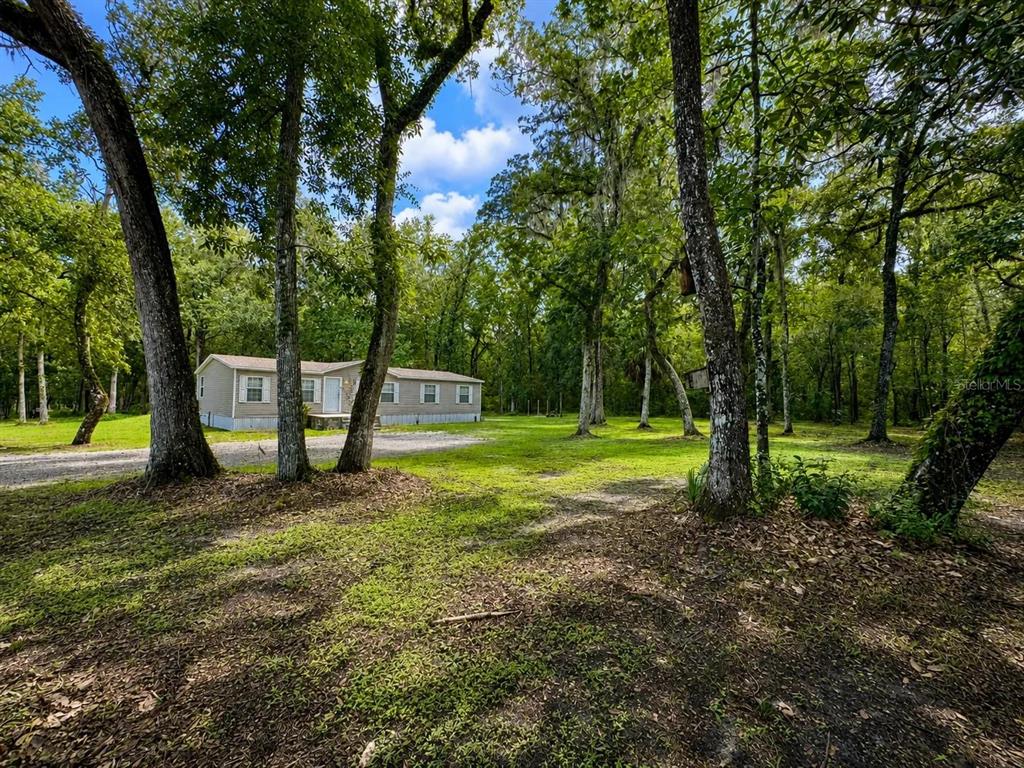 A single-story manufactured home sits on a wooded lot with a gravel driveway — 13539 CITRUS WAY, BROOKSVILLE, FL