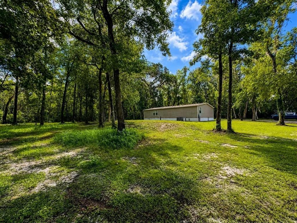 A tan mobile home sits in a grassy clearing surrounded by many tall trees — 13539 CITRUS WAY, BROOKSVILLE, FL