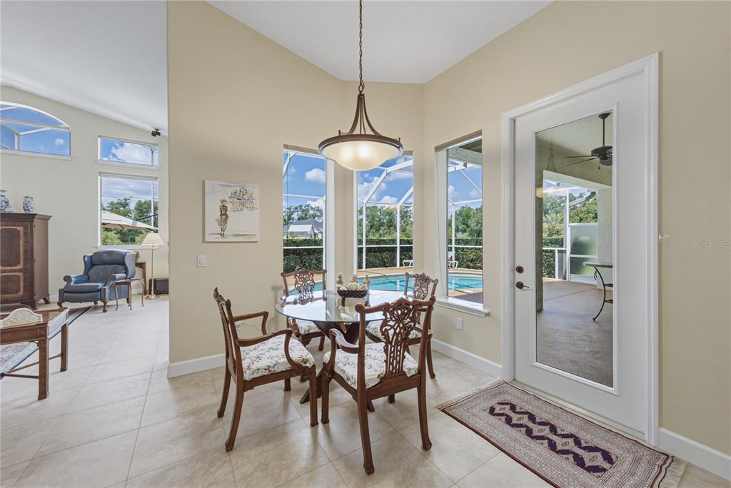 A dining nook features a glass-topped table, four chairs, and a view of a pool — 19616 AMAZON BASIN BEND, LUTZ, FL