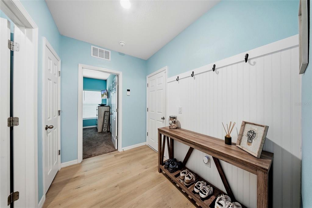 A hallway features light blue walls, wood-look flooring, a white beadboard wall with hooks, and a console table — 12953 CAMARILLO PLACE, LITHIA, FL