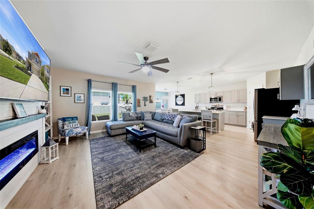 An open-concept living room features a grey sectional sofa, fireplace, and kitchen with light cabinetry — 12953 CAMARILLO PLACE, LITHIA, FL