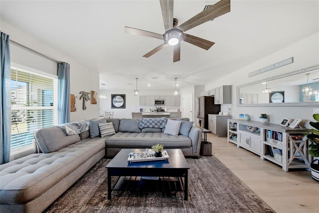 A living room with a gray sectional sofa, coffee table, and open kitchen in background — 12953 CAMARILLO PLACE, LITHIA, FL