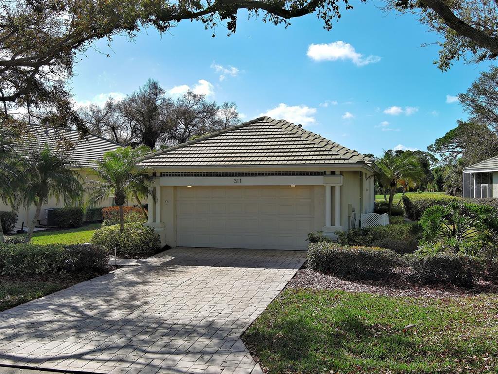 A beige house with a tiled roof and a paved driveway under a blue sky — 311 LANSBROOK DRIVE, VENICE, FL