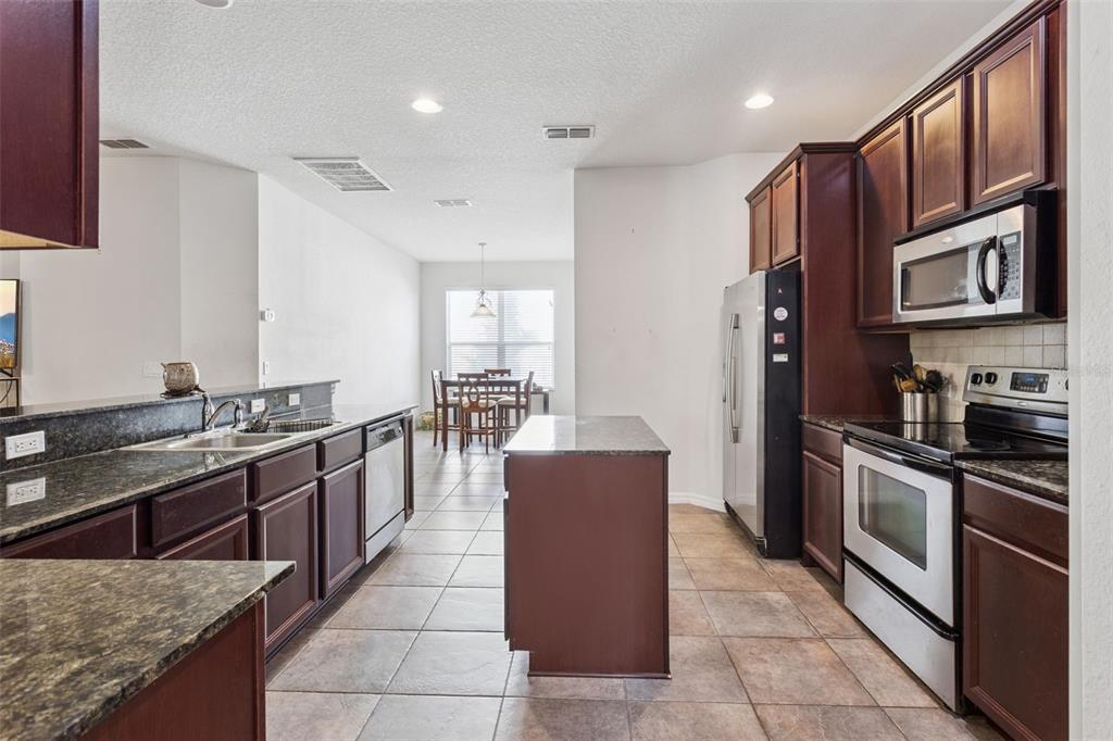 A kitchen with dark wood cabinets, granite countertops, stainless steel appliances, and an island — 30337 GIDRAN TERRACE, MOUNT DORA, FL