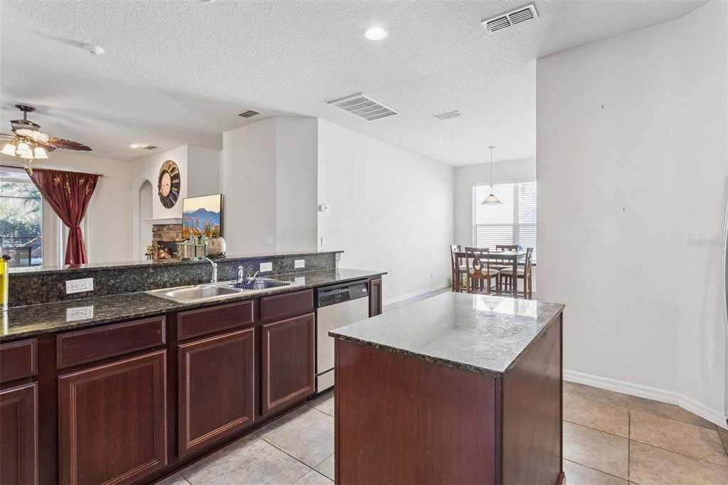 A kitchen with dark wood cabinets, granite countertops, a center island, and an adjacent dining area — 30337 GIDRAN TERRACE, MOUNT DORA, FL