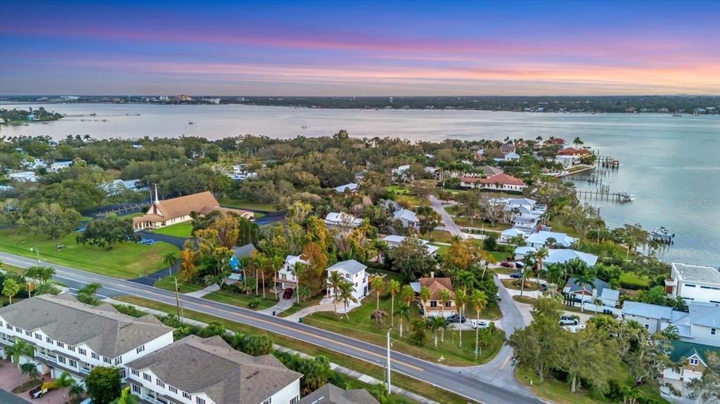 An aerial view shows a coastal neighborhood with houses, a church, and a large body of water — 3405 10TH STREET W, PALMETTO, FL