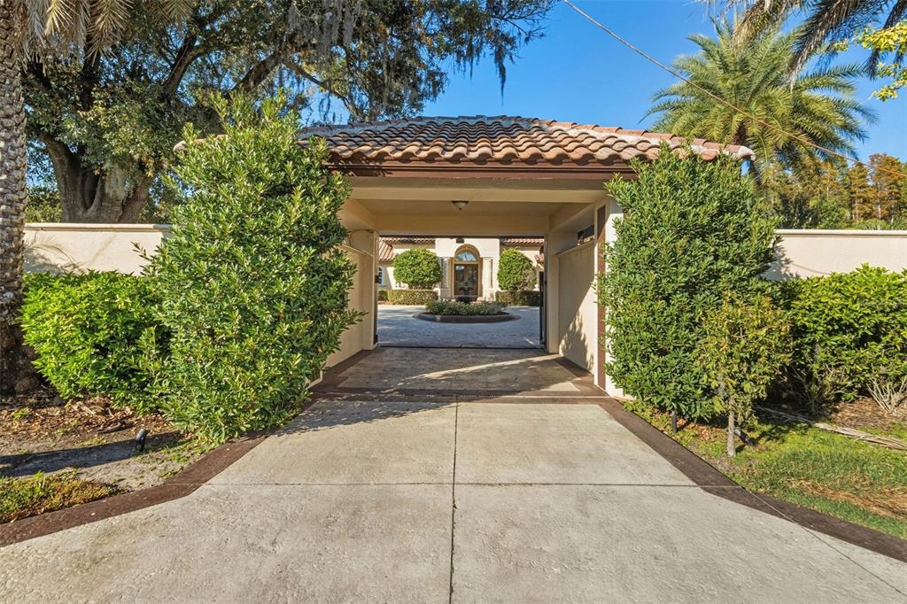 A concrete driveway leads through a covered entryway toward a gated courtyard with a fountain — 19165 GERACI ROAD, LUTZ, FL