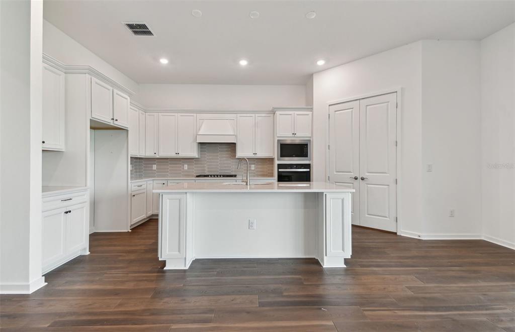 A modern kitchen features white cabinets, a central island, stainless steel appliances, and wood flooring — 17056 CANARY TRAIL, PARRISH, FL