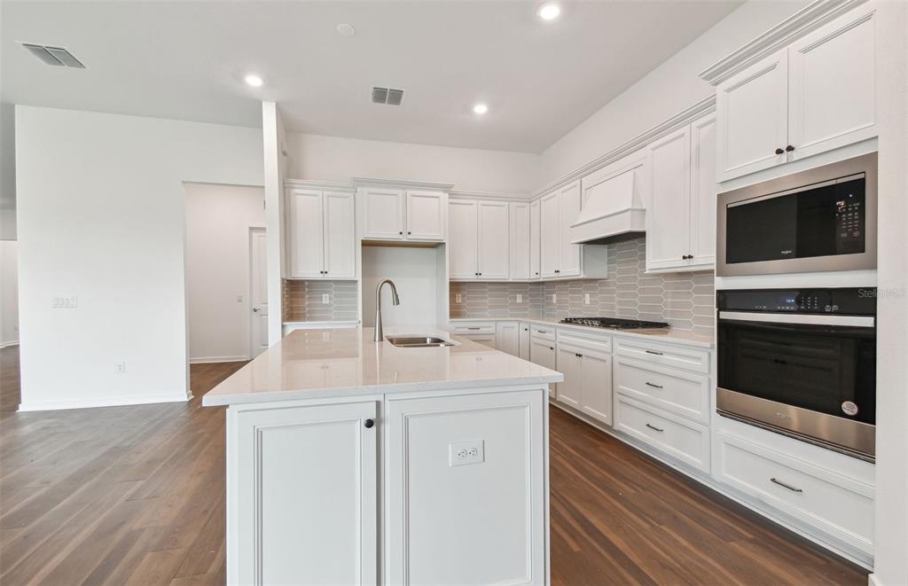 A modern kitchen features white cabinetry, a central island, stainless steel appliances, and wood flooring — 17056 CANARY TRAIL, PARRISH, FL