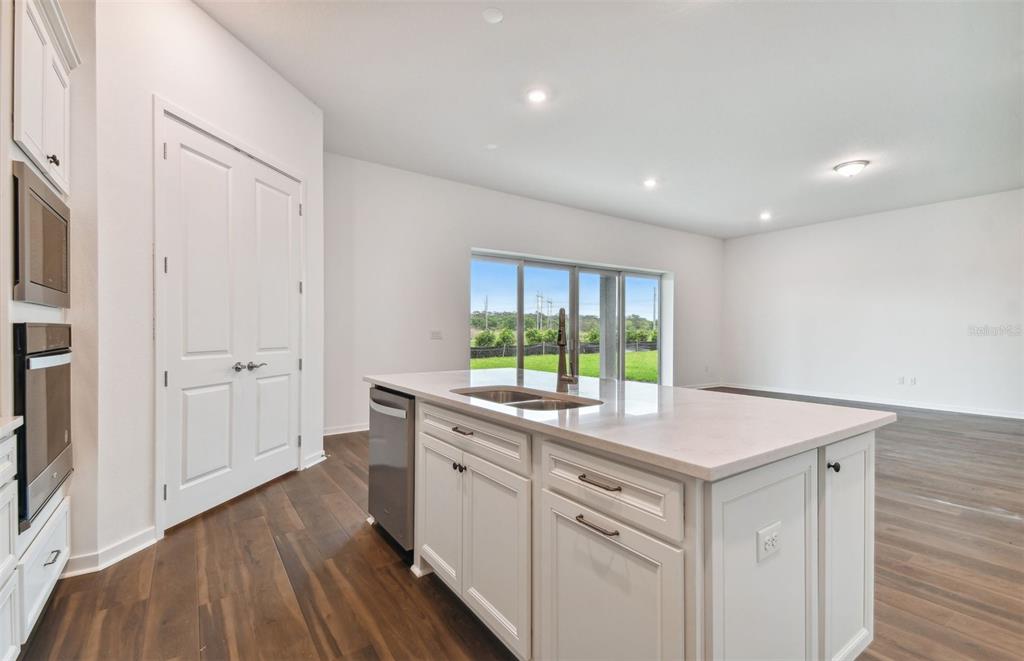 A kitchen island with a sink and dishwasher sits in a room with white cabinets — 17056 CANARY TRAIL, PARRISH, FL