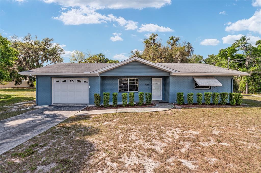 A single-story blue brick house with a garage, a front walkway, and a lawn — 9317 E CRESCENT DRIVE, INVERNESS, FL