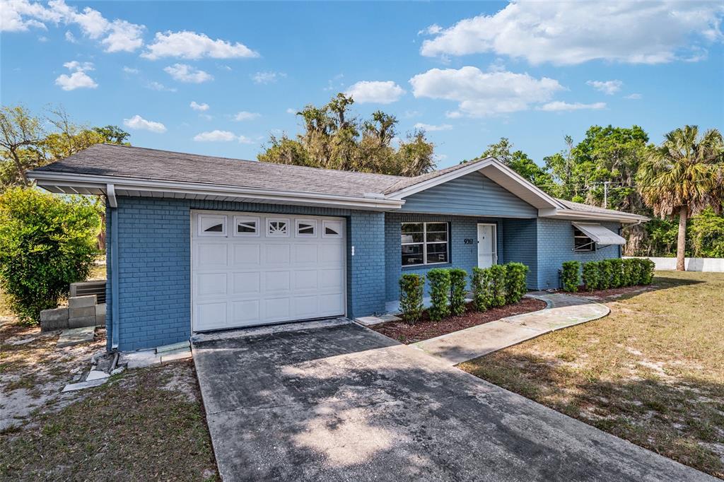 A blue brick single-story house features a white garage door and a concrete driveway — 9317 E CRESCENT DRIVE, INVERNESS, FL