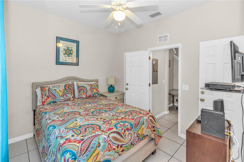 A bedroom features a bed with a colorful paisley comforter, tile flooring, and a ceiling fan — 712 CALABRIA AVENUE, DAVENPORT, FL