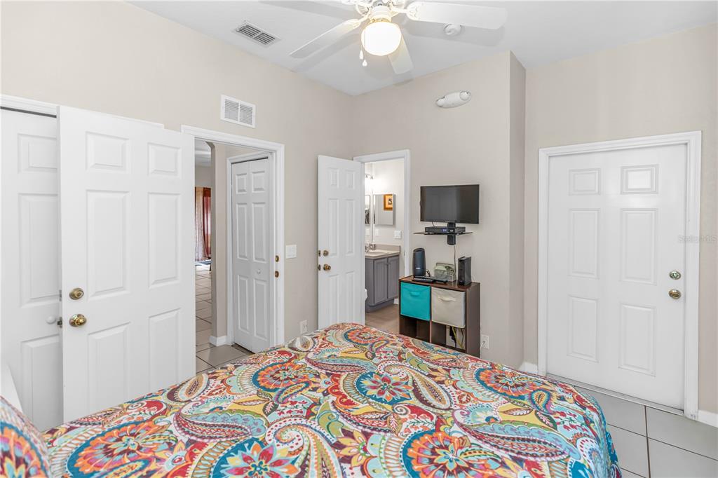 A bedroom features a patterned bedspread, a ceiling fan, tiled floors, and multiple white doors — 712 CALABRIA AVENUE, DAVENPORT, FL