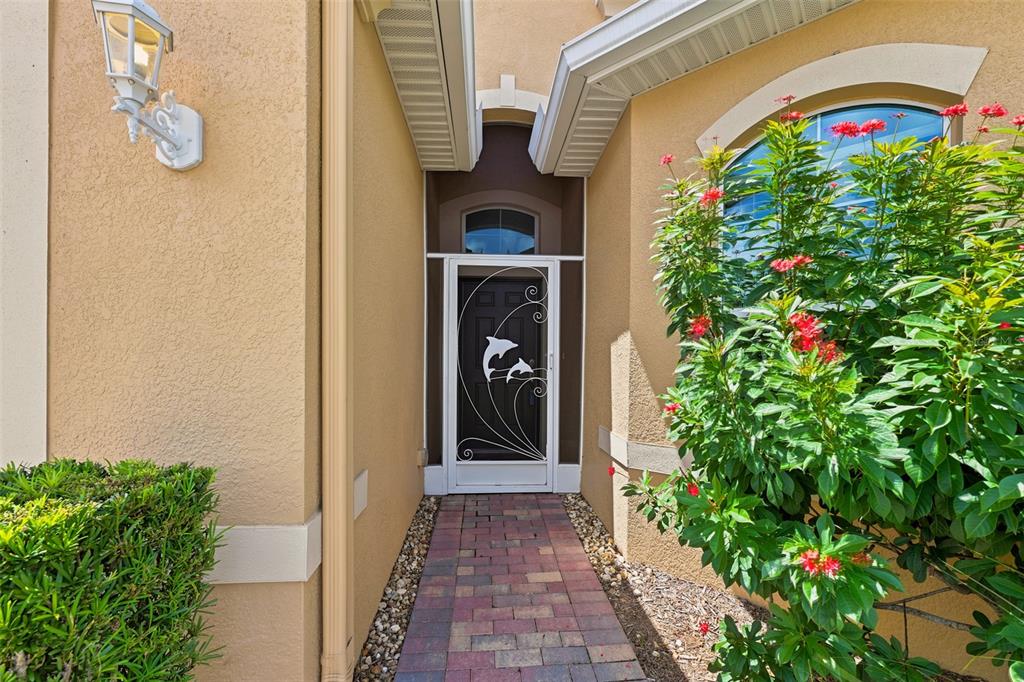 A paved walkway leads to a front door with a decorative dolphin-themed screen door — 623 CHIPPER DRIVE, SUN CITY CENTER, FL