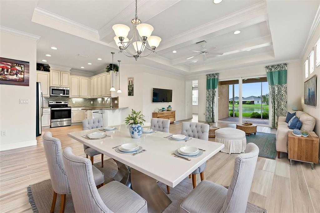 An open-concept dining area and living room with light wood floors and a tray ceiling — 623 CHIPPER DRIVE, SUN CITY CENTER, FL