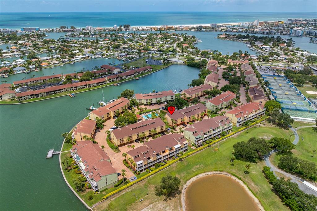 An aerial view shows a waterfront condominium complex with a swimming pool and tennis courts — 533 SANDY HOOK ROAD, TREASURE ISLAND, FL