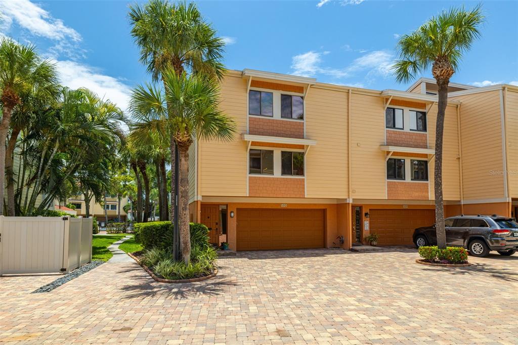 A three-story townhouse with tan siding, a brick-paver driveway, and two attached garages — 533 SANDY HOOK ROAD, TREASURE ISLAND, FL