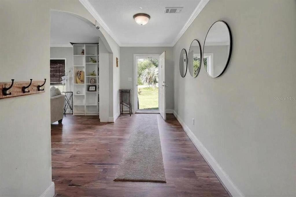 An entryway features wood-look flooring, three circular wall mirrors, and a white front door — 369 GARDEN LANE, BUNNELL, FL
