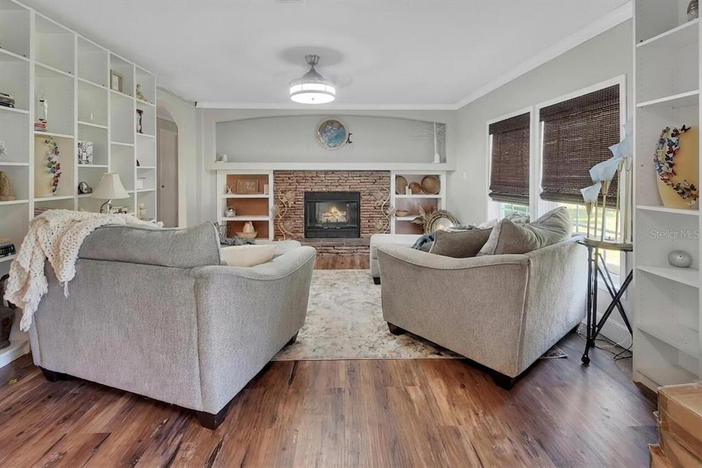 A living room features a brick fireplace, built-in shelving, two gray sofas, and wood flooring — 369 GARDEN LANE, BUNNELL, FL