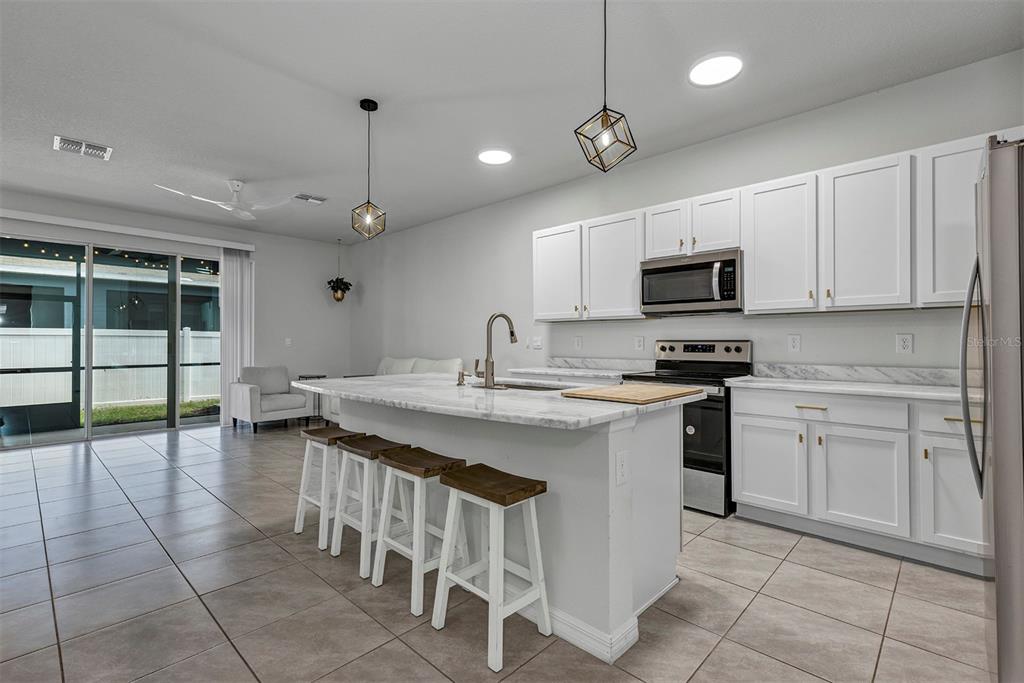 A kitchen features white cabinets, a marble-topped island with bar stools, and tiled flooring — 4015 BLUE BANKS LANE, BRADENTON, FL
