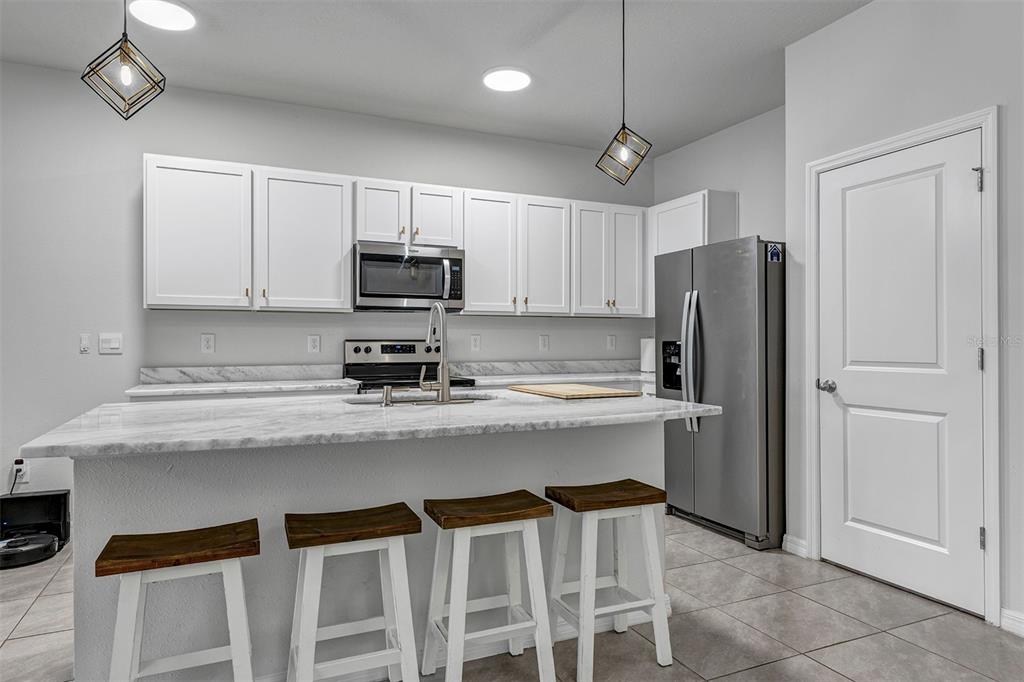 A kitchen features white cabinets, stainless steel appliances, a marble-topped island, and four bar stools — 4015 BLUE BANKS LANE, BRADENTON, FL