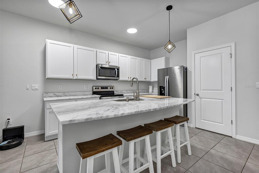 A kitchen features white cabinets, marble-look countertops, a central island with stools, and stainless appliances — 4015 BLUE BANKS LANE, BRADENTON, FL