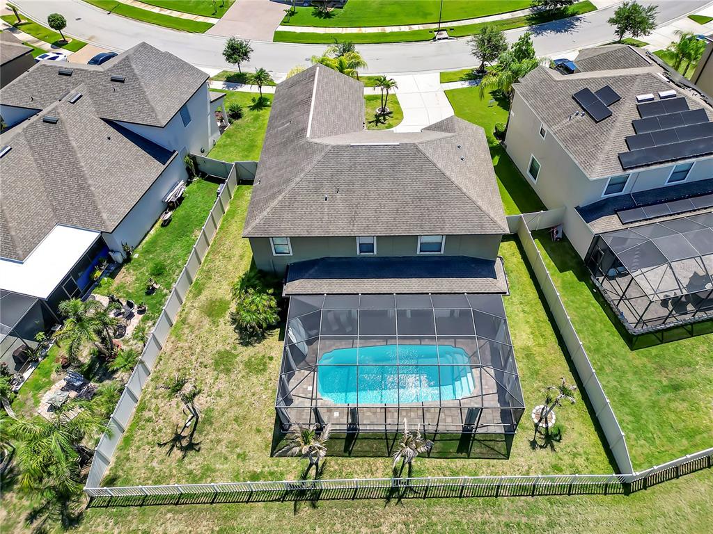 A screened-in swimming pool with a paver deck overlooks a pond and neighboring houses — 5063 IVORY STONE DRIVE, WIMAUMA, FL