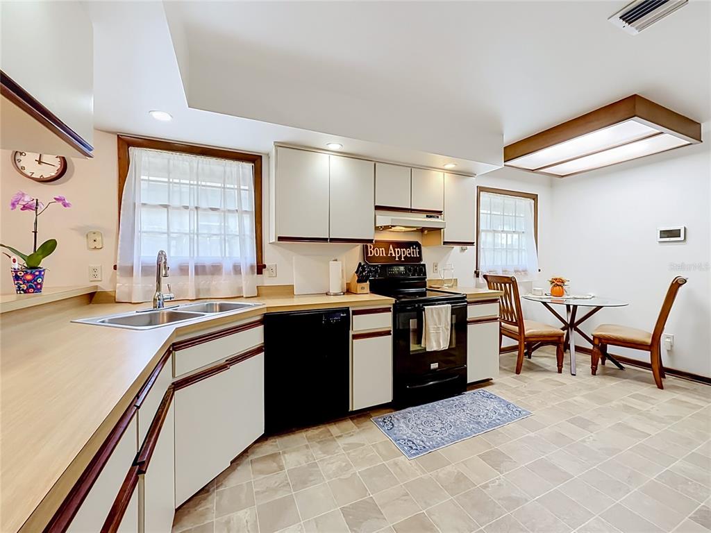 A kitchen with white cabinets, black appliances, laminate countertops, and a small dining area — 7104 BLEDSOE AVENUE, ORLANDO, FL
