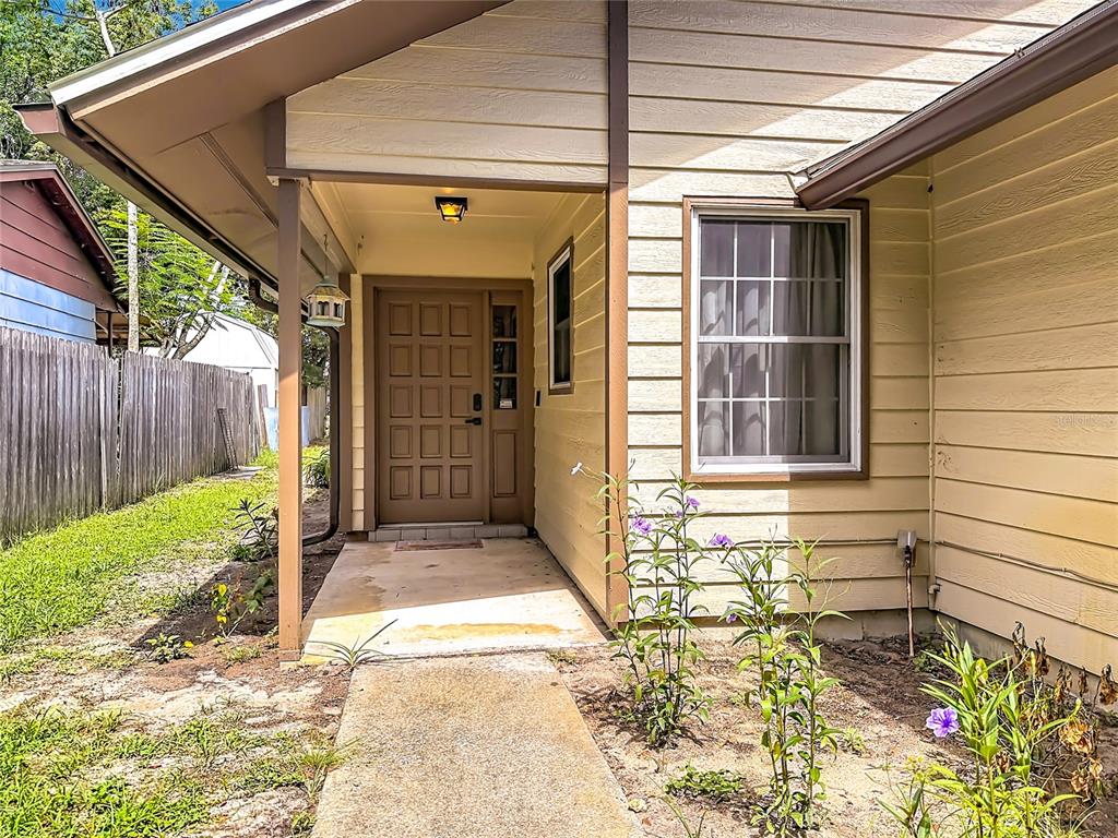 The exterior of a house features a tan front door, a concrete walkway, and landscaping — 7104 BLEDSOE AVENUE, ORLANDO, FL